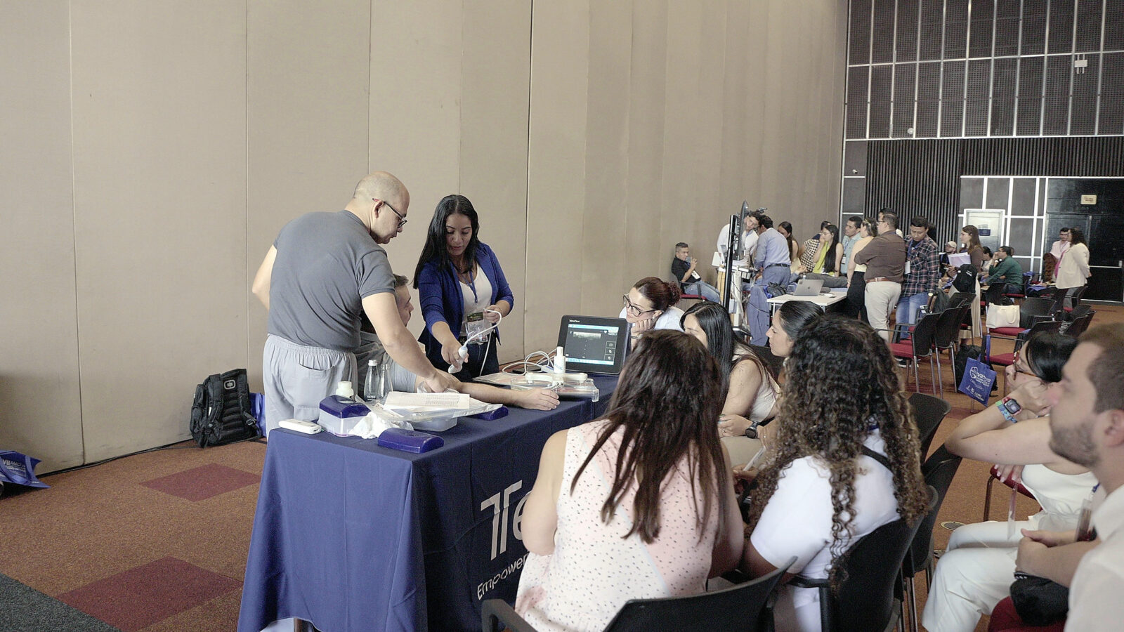 Demostración de ecografía en un stand de la muestra comercial ante asistentes sentados.