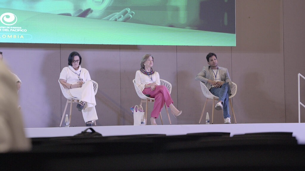 Panelistas conversan sentados en el escenario del auditorio principal.